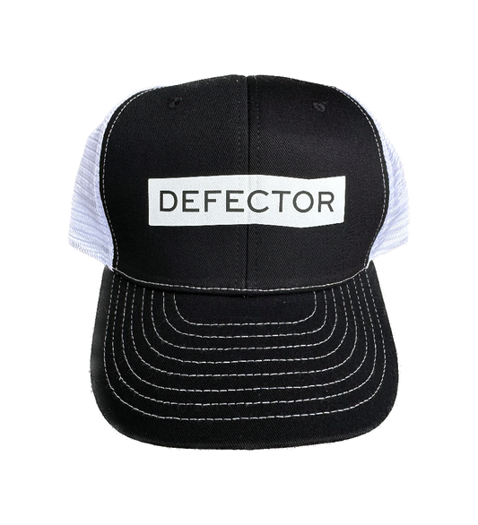 Defector black trucker hat with white Defector logo printed in the center of the front. Back mesh is white.